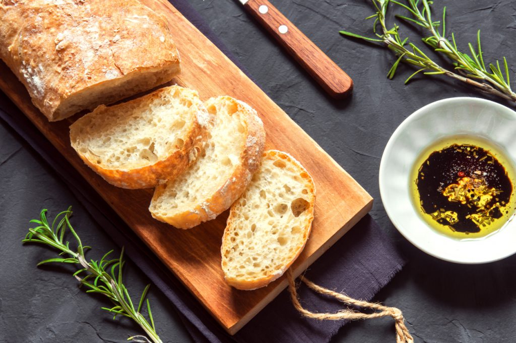 Italian bread Ciabatta with olive oil and rosemary on black background - fresh